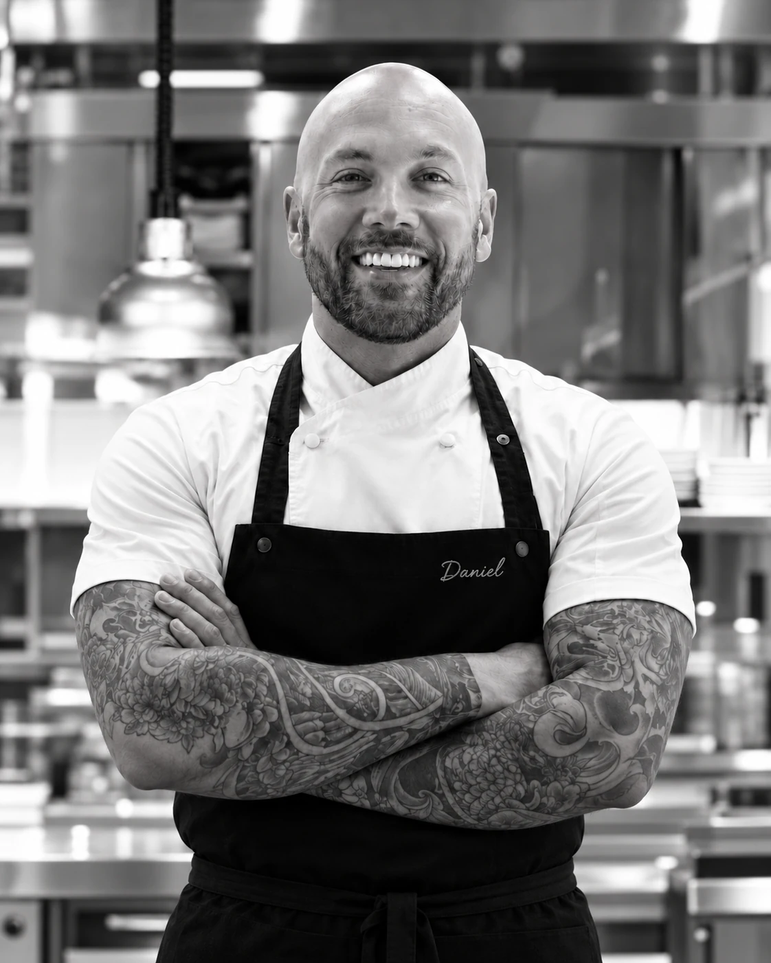 Daniel James in a chef jacket and black apron with subtle name embroidery